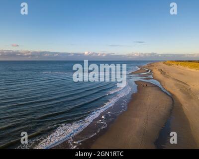 Aerial view of three people riding galloping horses on the beach near the Westerduinen dunes along the North Sea coast at sunset, near Den Hoorn, Texe Stock Photo