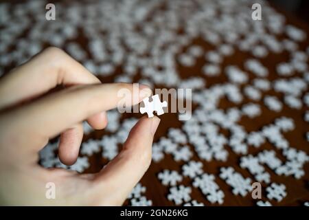 Left hand holding a piece of white jigsaw puzzle Stock Photo