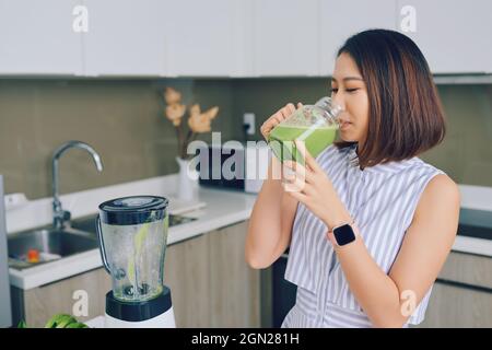 Asian woman drinking smoothie in the kitchen. Healthy concept. Stock Photo