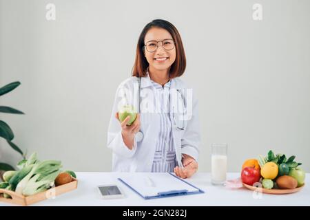 Smiling nutritionist in her office, she is showing healthy vegetables and fruits, healthcare and diet concept. Stock Photo