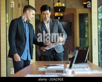 Two businessmen working together in a meeting room, looking at a financial report graph for forecasting business budget. diverse business people Stock Photo
