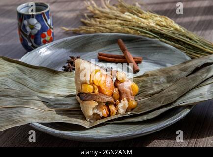 Chinese rice dumplings (Zongzi) shaped pyramidal wrapped by leaves ingredients on bowl chinese style and chopsticks served with chinese tea. Famous as Stock Photo