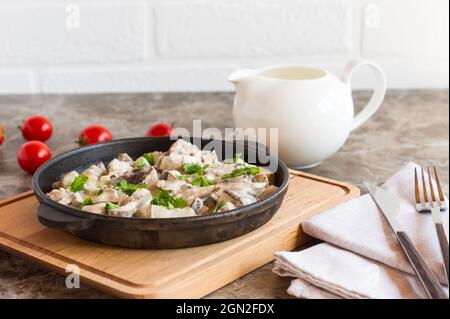 stewed mushrooms in sour cream and parsley in a frying pan on a wooden stand Stock Photo