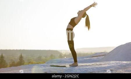 Young fitness woman doing yoga outdoors at sunset. backbend stretching training Stock Photo