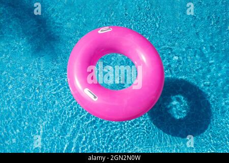 Summer background with pink inflatable ring donut in blue swimming pool. Top view. Hot sunny vacation concept - Image Stock Photo