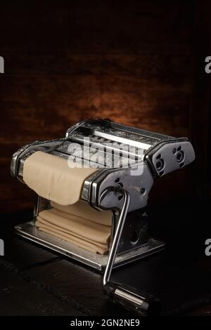 Metal machine for preparing spaghetti with raw pastry placed on wooden table on dark background in studio Stock Photo
