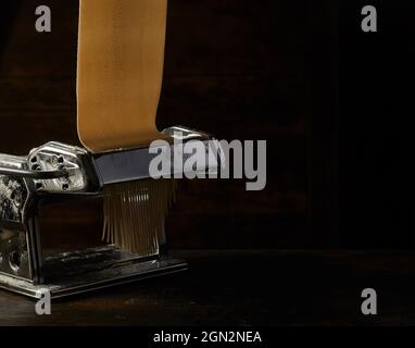 Metal machine with raw pastry for making spaghetti placed on wooden table on black background in studio Stock Photo