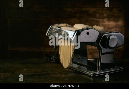 Modern steel machine for making spaghetti from raw pastry placed on wooden table in dark studio Stock Photo