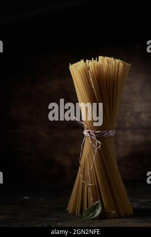 Bunch of dried spaghetti and green basil leaf served on table on black background in studio Stock Photo