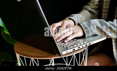 Close-up of woman's hands in a jacket typing on a laptop computer. The person works, studies at home online. No face. Stock Photo