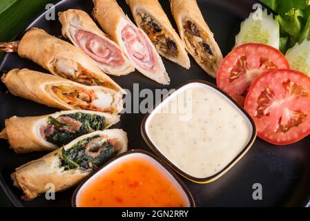 black plate with a fusion of spring rolls dispalyed with dipping sweet chilli sauceand mayonaise Stock Photo