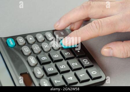 The man's index finger presses the green plus key of the calcula Stock Photo