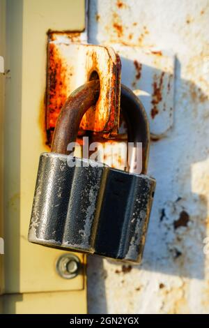 Closed padlock hanging on the hinges on a gray rusty iron door Stock Photo