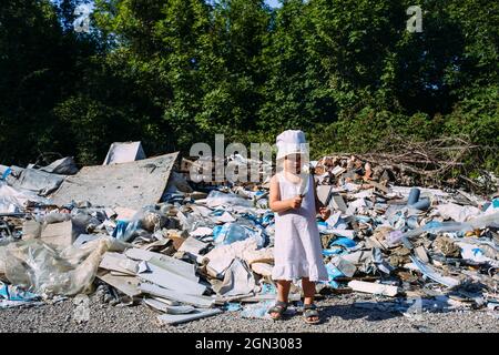 Little girl at a dump among a heap of scattered garbage in the forest.  Stock Photo