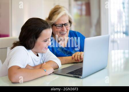 Smiling granddaughter and grandmother sitting at table and using laptop in light room in apartment Stock Photo