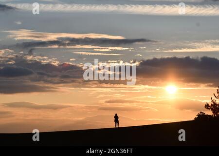Silhouette of a woman standing on a hillside looking out onto an array of cloud formations in the sky with an autumnal sunshine setting Stock Photo