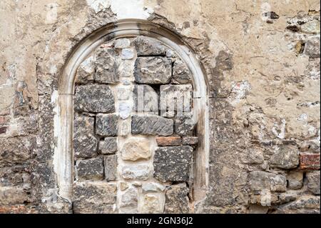 Historic facade with ancient building entrance or window, temporarily walled up with various stones. Stock Photo