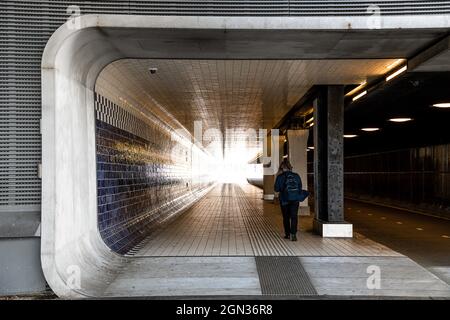 Back view full body of anonymous pedestrian walking on tiled passage near asphalt road under lamps Stock Photo