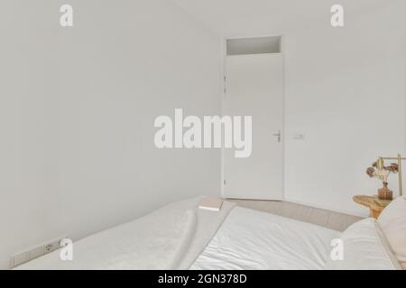 Empty light bedroom with comfortable bed and bedside table with vase with flowers in daytime Stock Photo