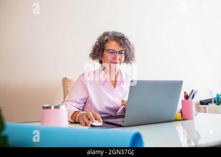 Female senior entrepreneur with tablet and netbook working at desk with graphics on paper sheets Stock Photo