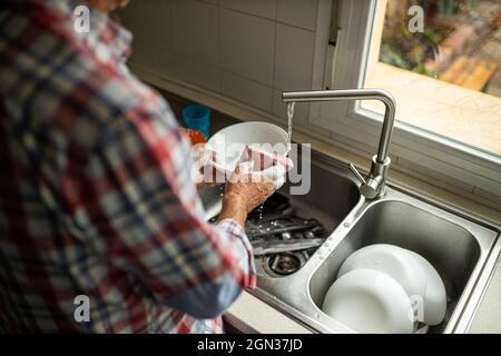 Side view of cropped unrecognizable male washing dirty plates while standing near sink in kitchen and doing housework Stock Photo