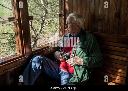 man taking photos with his old camera through the window of an old wooden train car Stock Photo