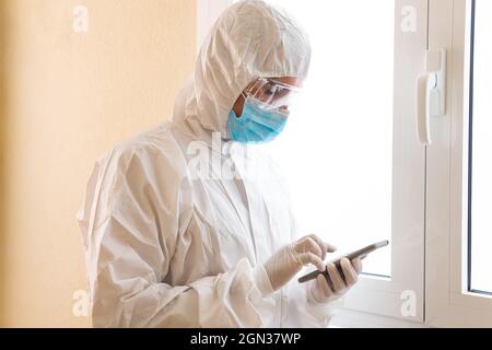 Unrecognizable male medic in personal protective equipment touching screen on smartphone during COVID 19 pandemic in clinic Stock Photo