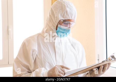 Adult male medic in personal protective equipment reading paper on clipboard during COVID 19 pandemic in hospital Stock Photo