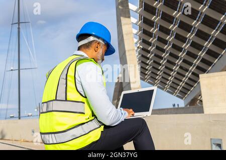 Anonymous male supervisor in uniform working on netbook sitting near solar power station Stock Photo