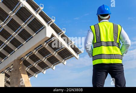 Low angle back view of unrecognizable male inspector in vest with protective helmet against modern solar power station Stock Photo