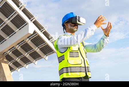 Low angle of bearded male inspector in uniform exploring virtual reality in headset against modern construction under cloudy sky Stock Photo