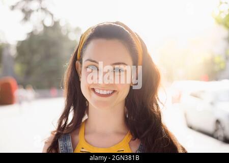Young happy female with long brown hair wearing denim overall standing looking at camera with smile Stock Photo