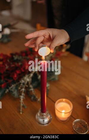 Crop unrecognizable Woman lightning candle placed on wooden table with Christmas decorations in room Stock Photo