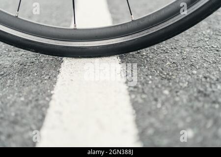 Bike wheel with spokes on rough roadway with marking line in daylight on blurred background Stock Photo