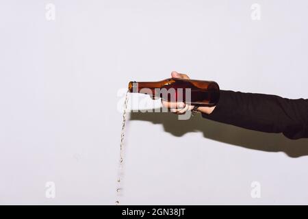Crop anonymous male pouring beer from transparent glass bottle at party against white background Stock Photo