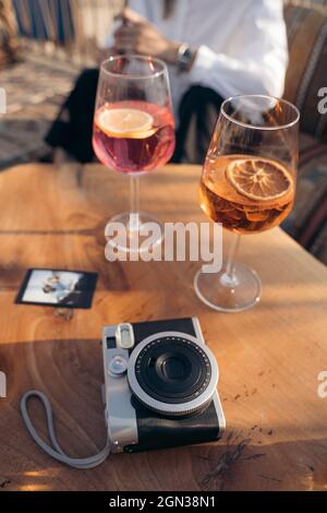 From above of instant photo camera with photo and cocktails on wooden table near crop anonymous man Stock Photo