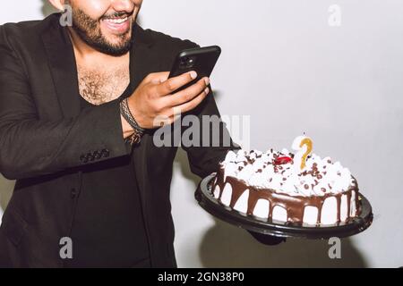 Crop cheerful male with mouth opened taking picture of delicious birthday cake during party Stock Photo