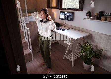 Young ethnic female trader putting on wireless headphones before analyzing cryptocurrency graphics on computer monitor in house Stock Photo