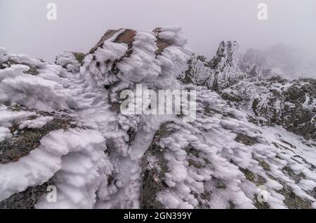 Snow on rocky formation of mountain range located in Sierra de Guadarrama National Park in hazy weather Stock Photo