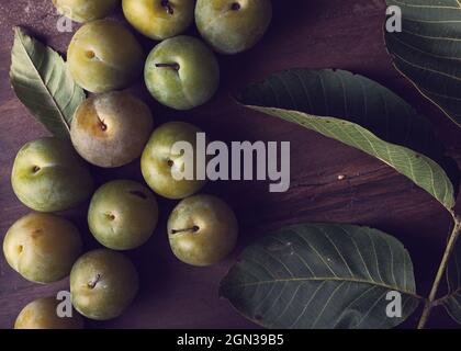 From above of fresh ripe plums and green leaves placed on wooden table in daytime Stock Photo