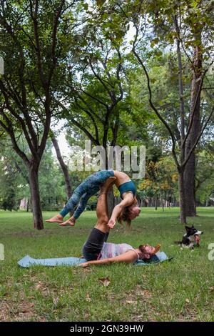 Side view of flexible couple in sportswear practicing acroyoga together on yoga mat on grass against trees in park in daytime Stock Photo