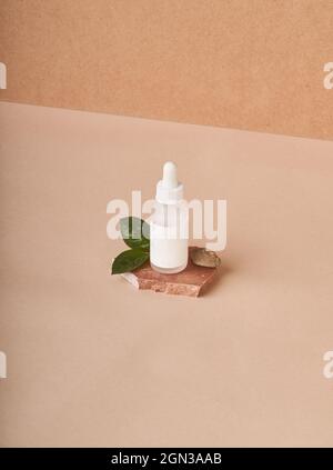 Small white bottle of cosmetic serum placed on stacked brown marble stone pieces on fabric on beige background Stock Photo