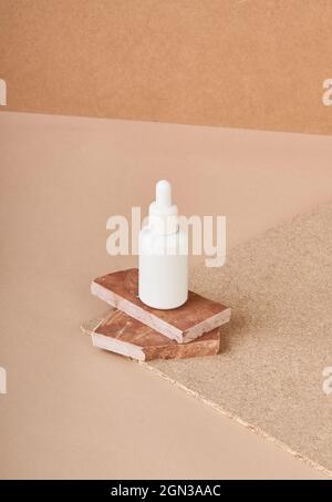 Small white bottle of cosmetic serum placed on stacked brown marble stone pieces on fabric on beige background Stock Photo