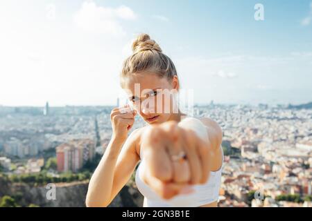 Female boxer shouting while showing hitting technique and looking at camera during workout in sunny city Stock Photo