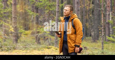 Middle-aged man with smartphone in the coniferous autumn forest. Hiker - man hiking in forest - Image Stock Photo