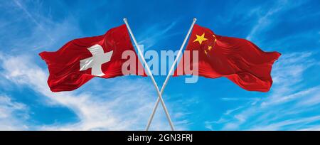 flags of China and switzerland waving in the wind on flagpoles against sky with clouds on sunny day. Symbolizing relationship, dialog between two coun Stock Photo