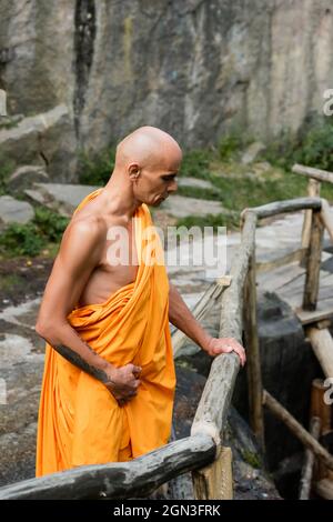Tattooed Buddhist In Traditional Orange Robe Meditating On Hill In Tattooed Buddhist In Traditional Orange Robe Meditating On Hill In