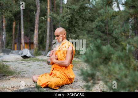 buddhist monk in orange robe meditating with closed eyes in lotus pose Stock Photo