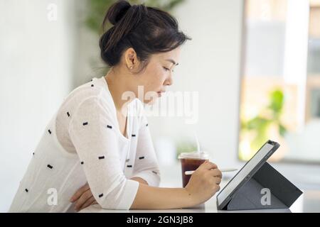 Asian female working on her tablet and drinking coffee Stock Photo