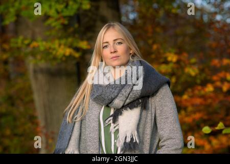 Beautiful young woman in nature, wearing a warm nice scarf and enjoying some relaxed quality time in autumn, with colorful foliage in the background Stock Photo